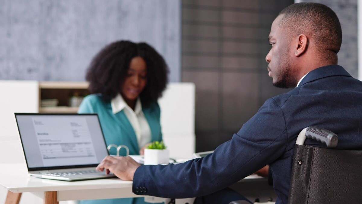A man in a wheelchair uses a laptop at a deskv