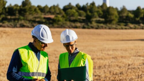 Two employees in hard hats work from a field
