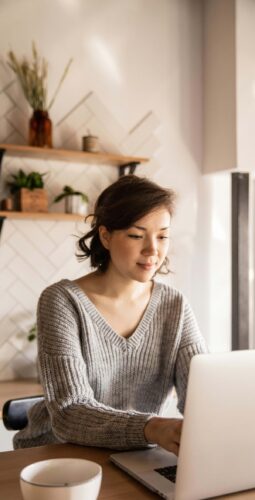 A young woman in a cozy, home environment; she is working on a laptop