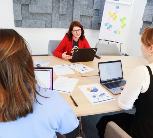 Three young women around a table review charts and use their laptops