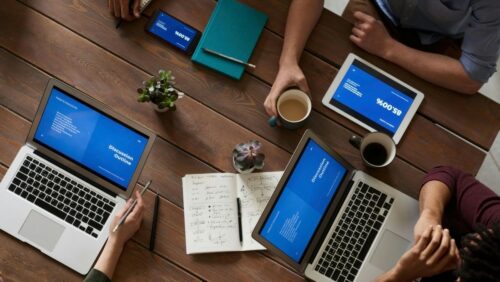 An flat-lay view of a group of people working on laptops, phones, tablets and drinking coffee; succulents rest on the table