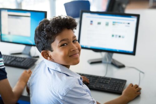 A young student is using a computer and smiling back at the camera